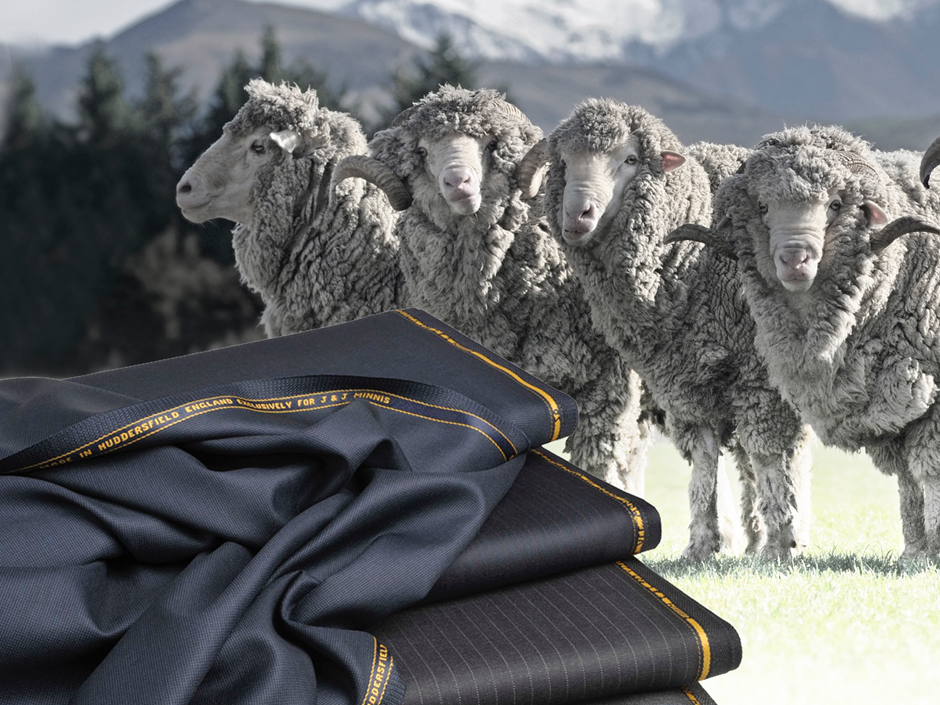 Four sheep in a meadow with snow-capped mountains in the background. In the foreground to the left is a pile of fabrics